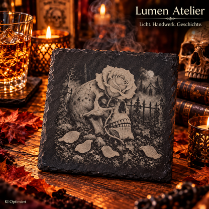 Quadratischer Schieferuntersetzer mit Lasergravur eines seitlich dargestellten Totenschädels, einer großen Rose, verstreuten Blütenblättern und einem Friedhof im Hintergrund.